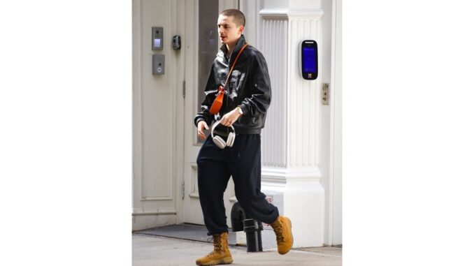 Timothée Chalamet spotted with Apple AirPods Max— discounted on Amazon Timothée Chalamet walking on a street, wearing a black jacket, dark sweatpants, brown boots, and an orange shoulder bag, holding white headphones.