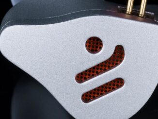 Close-up of a silver metallic device with a perforated orange grille and two gold connectors on top.