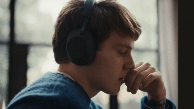 A young boy wearing a pair of blue headphones and blue jumper holding his hand up against his mouth