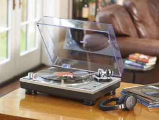 the Audio-Technica AT-LP120XUSB record player photographed on a wooden table with a raised dust cover and playing a vinyl