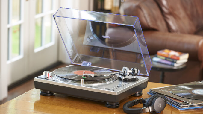 the Audio-Technica AT-LP120XUSB record player photographed on a wooden table with a raised dust cover and playing a vinyl
